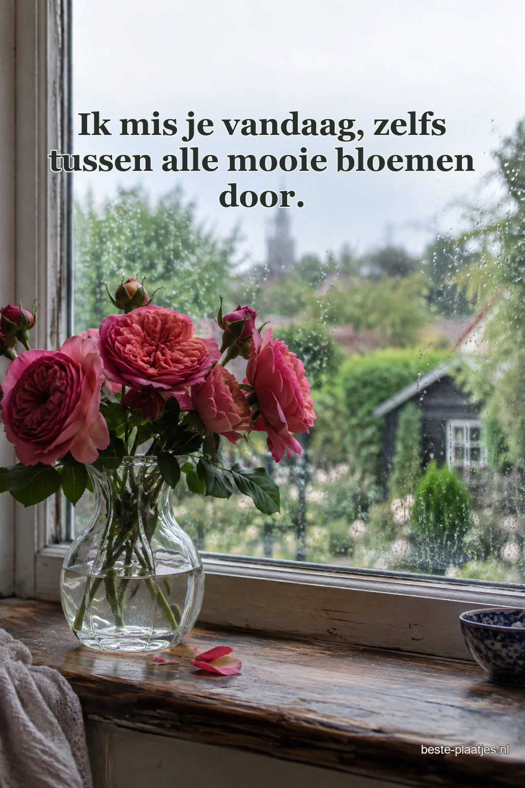 Een glazen vaas met rozerode rozen staat op een houten vensterbank voor een regenachtige tuin.
